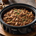 slow cooked pulled pork in crock pot surrounded by herbs